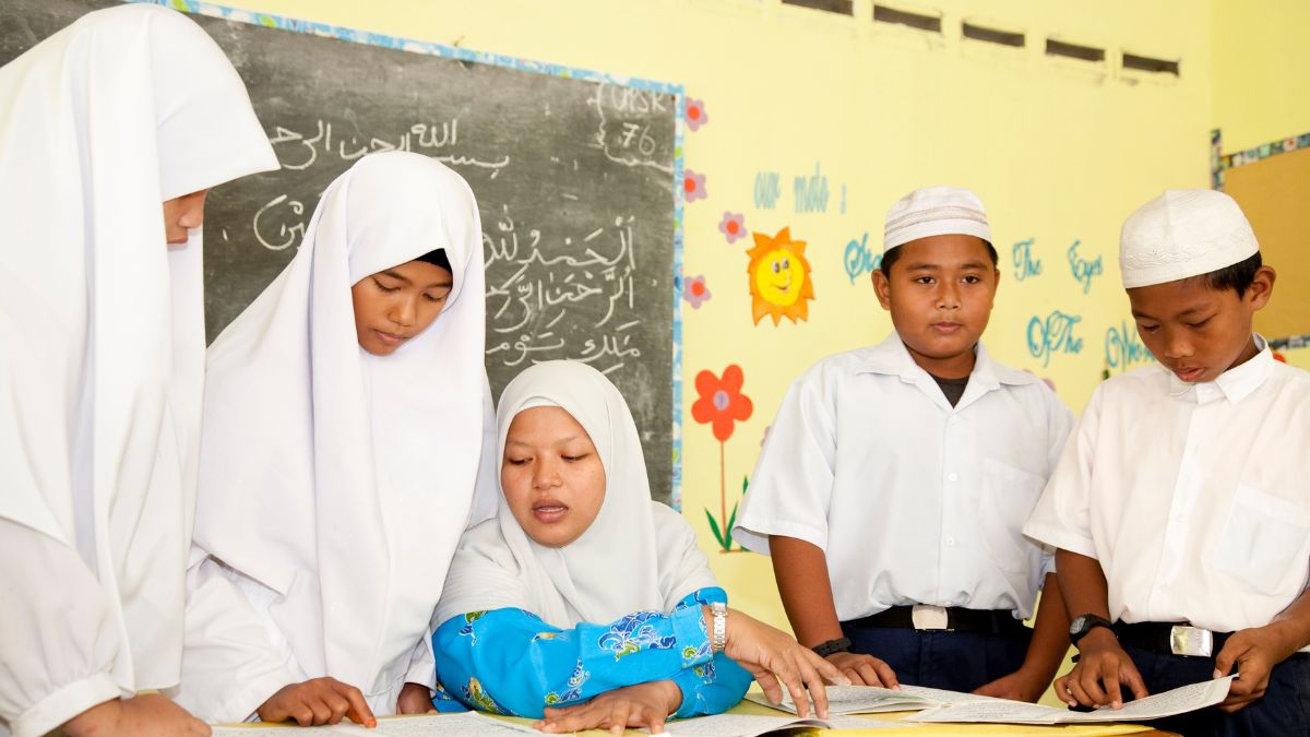 Guru mengajar di kelas dengan siswa yang fokus mendengarkan pelajaran.