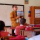 Guru sedang mengajar di kelas dengan latar belakang papan tulis, melambangkan penerima tunjangan sertifikasi.